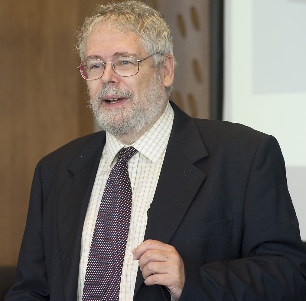 Photo of Jaime Carbonell in a suit, speaking in front of a presentation