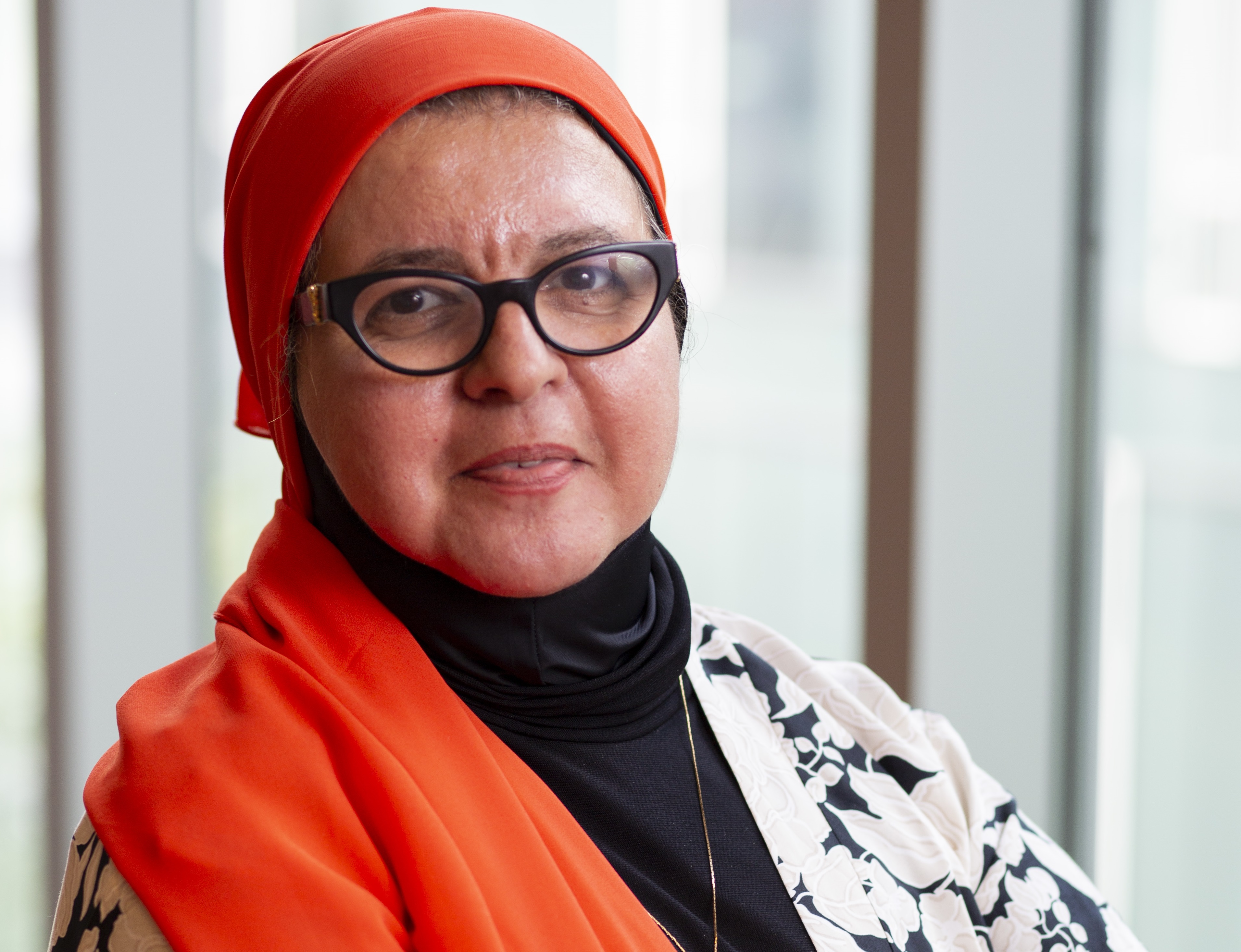 A headshot of Mona Diab, crossing her arms and wearing an orange hijab