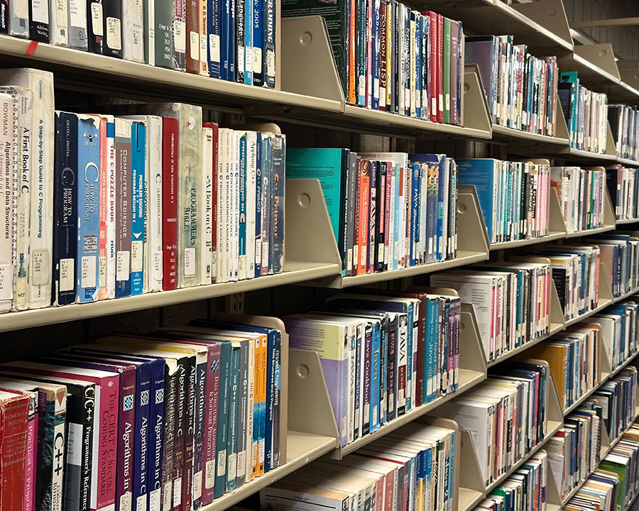 A photo of a library aisle showing several stacks with multiple shelves each filled with books.
