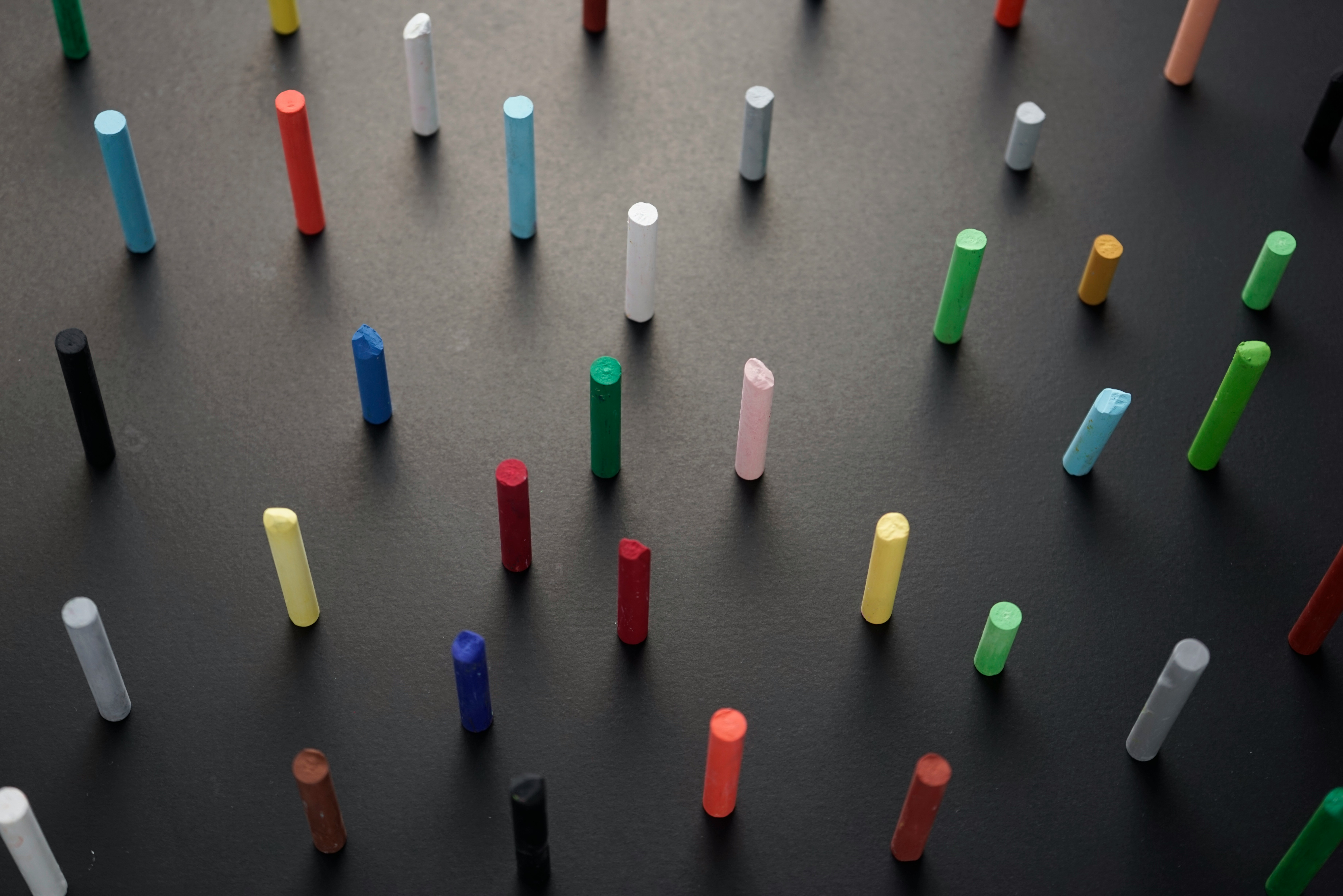 A variety of colorpul pieces of chalk stand upright on a dark grey surface